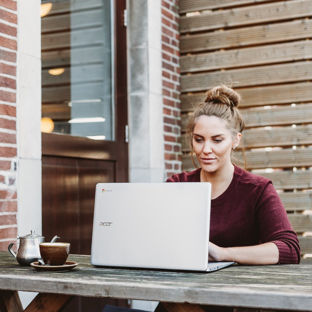 woman sitting and holding white Acer laptop near brown wooden wall